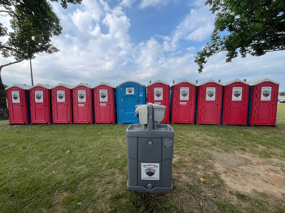 A row of S2S red and blue portable restrooms with a handwashing station on grass