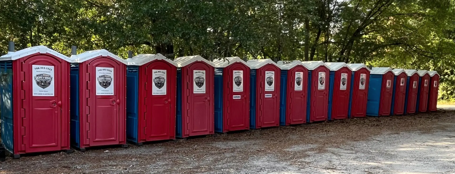 A row of authentic S2S branded portable restrooms along a wooded equipment area